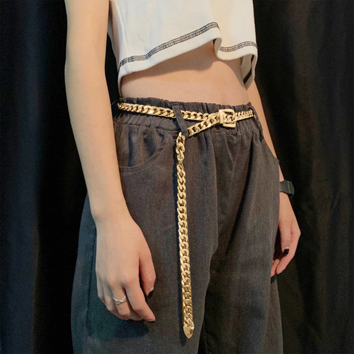 Ceinture chaîne Ceintura dorée à maillons portée sur un pantalon gris, pan de chaîne retombant sur le côté