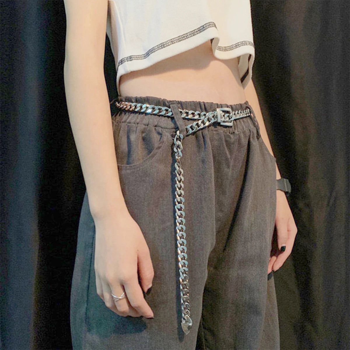 Ceinture chaîne Ceintura argentée à maillons portée sur un pantalon gris, pan de chaîne retombant sur le côté