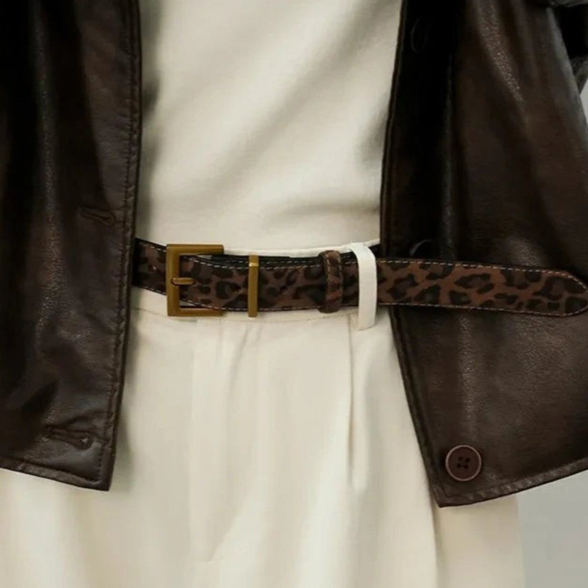 Ceinture Ceintura Positano en daim léopard portée à la taille sur un pantalon blanc, boucle dorée