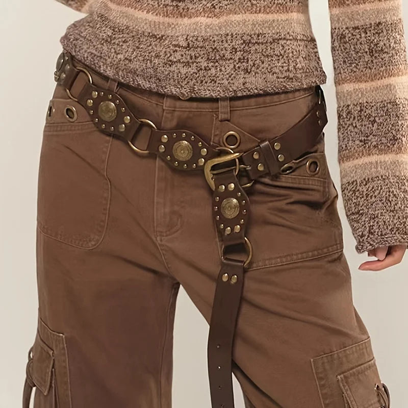 Ceinture Ceintura Gubbio marron à conchos dorés portée bas sur un pantalon cargo, sangle libre retombante