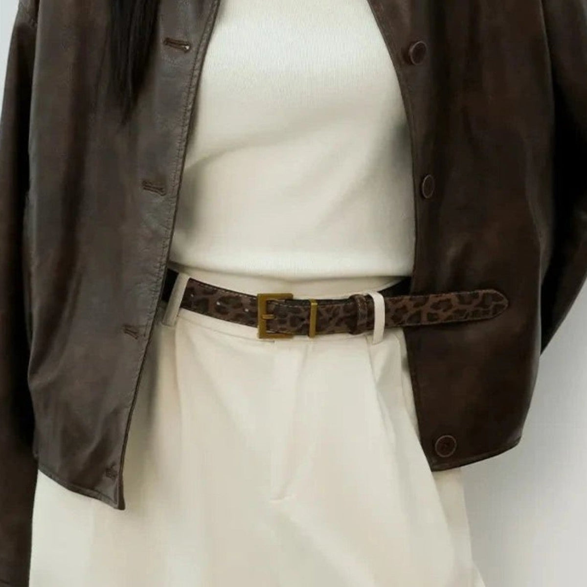 Ceinture léopard Ceintura Positano portée sur un pantalon blanc avec une veste en cuir marron