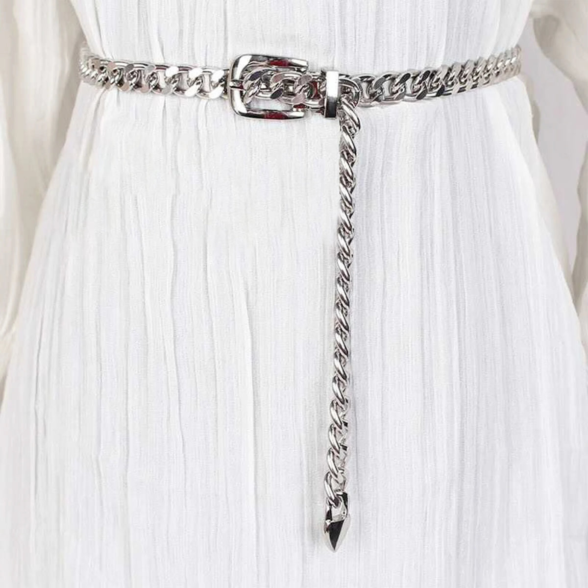 Ceinture chaîne Ceintura argentée portée sur une robe blanche, boucle ardillon et embout pointu pendant
