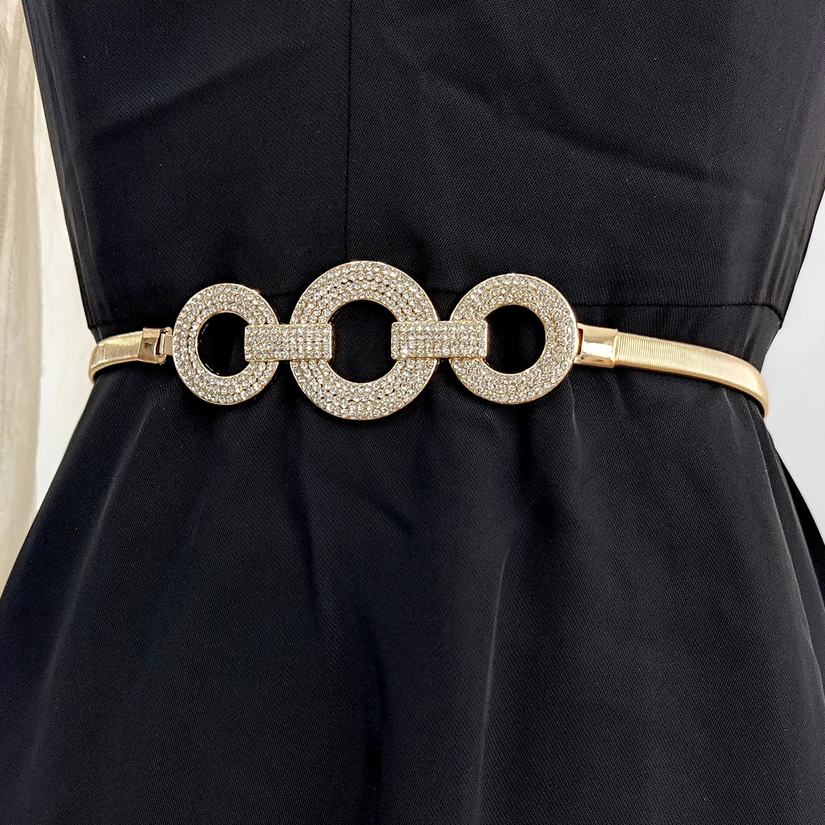 Ceinture bijoux élastique Ceintura Cefalù dorée fine avec trois anneaux ornés de strass sur une robe noire Image