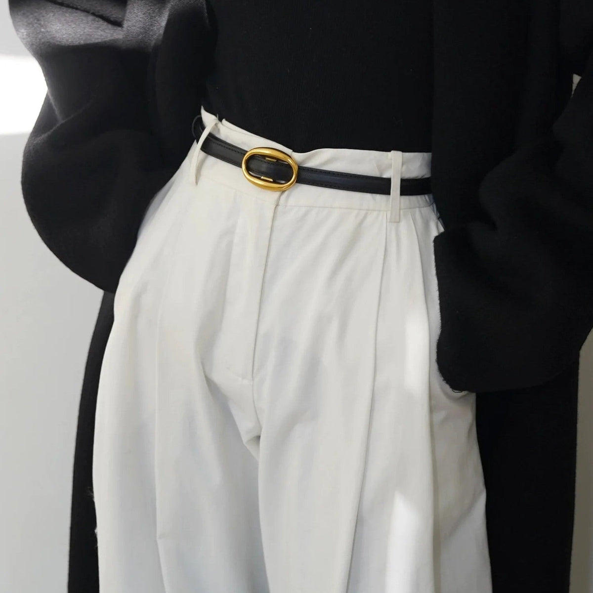 Ceinture Ceintura Capri fine en cuir noir avec boucle ovale dorée portée sur un pantalon blanc
