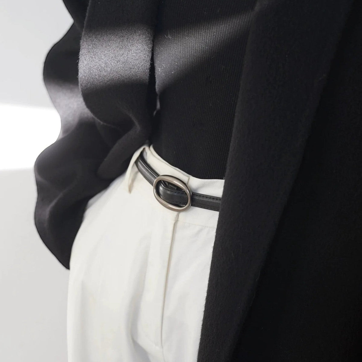 Ceinture Ceintura Ravello fine en cuir noir avec boucle ovale en argenté brossé portée sur un pantalon blanc Image