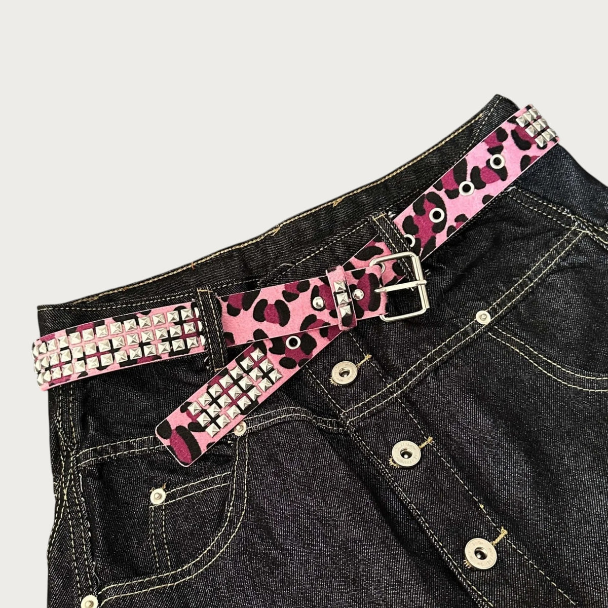 Ceinture Ceintura style Y2K à imprimé léopard rose et noir avec clous pyramidaux métalliques sur un jean noir Image
