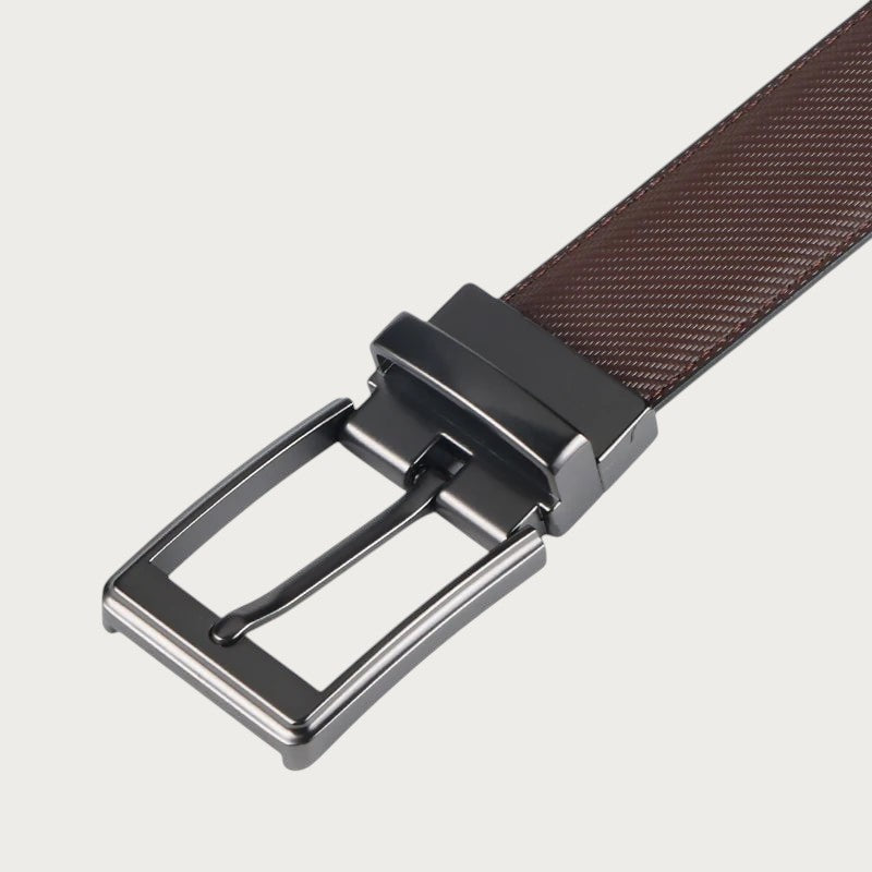 Gros plan sur la boucle rotative en métal foncé et le cuir marron grainé de la ceinture réversible Ceintura