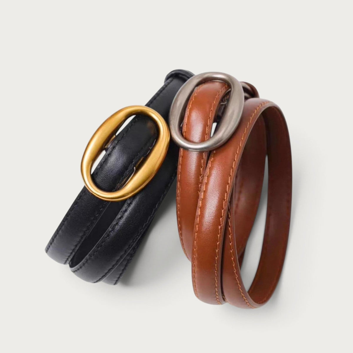 Ceintures en cuir Ceintura Capri, l'une noire à boucle dorée et l'autre marron à boucle argentée, design minimaliste.